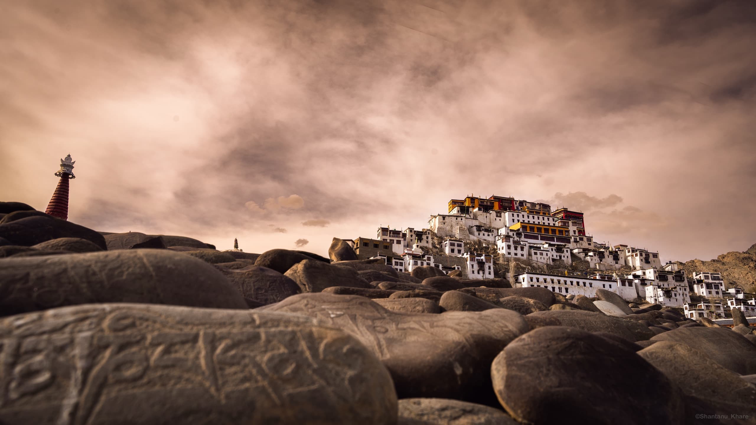 Travel photography — Thiksey Monastery above carved mani stones under a dramatic sky, Ladakh.