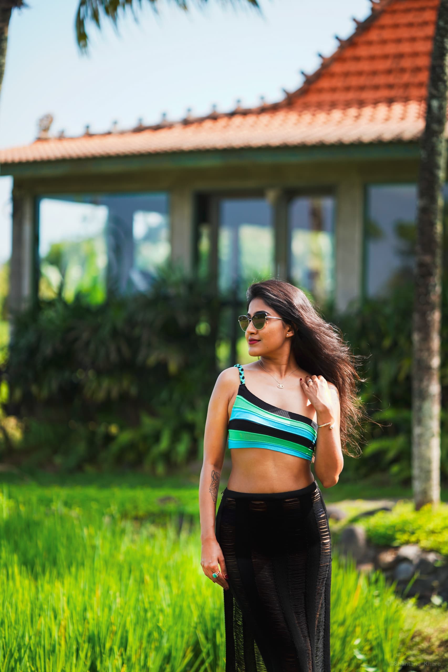 Portrait photography — a woman in sunglasses beside a villa wrapped in rice-green fields.