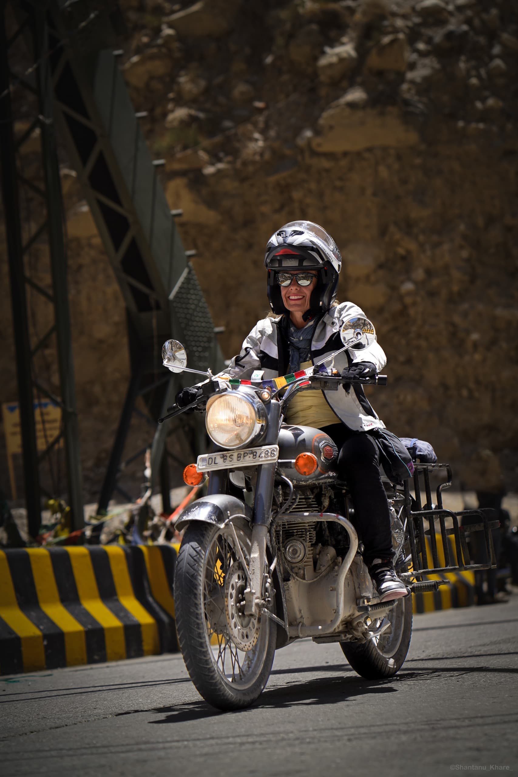 Travel photography — a rider on a Royal Enfield motorcycle crossing a mountain bridge.