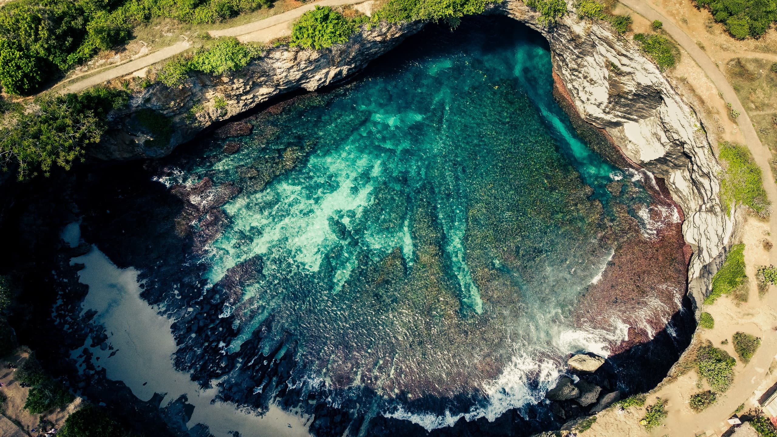 Aerial drone photography — a turquoise tidal pool carved into dark coastal rock, Nusa Penida, Bali.