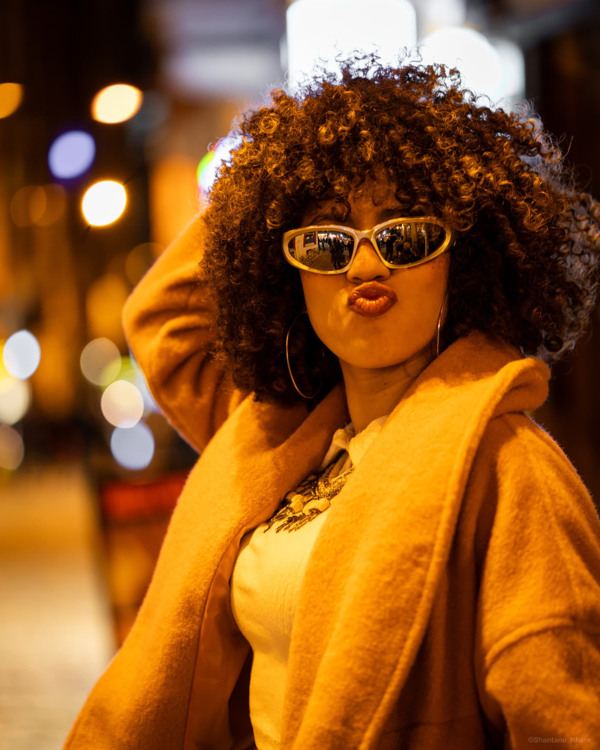 Night portrait photography — a woman in a mustard coat amid glowing city bokeh.